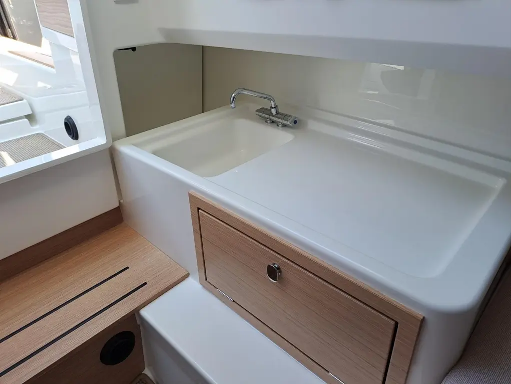 Modern boat interior featuring a sleek white sink, wooden cabinetry, and natural light from a nearby window.